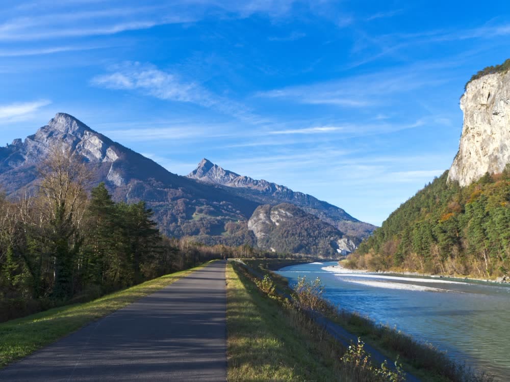 A paved cycle path along a river below the mountains